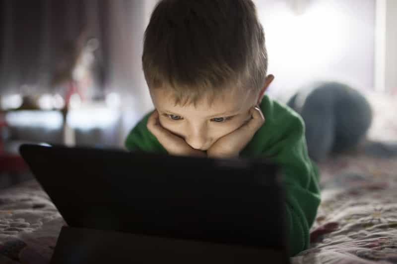Criança com roupa verde assistindo atentamente algo no tablet.